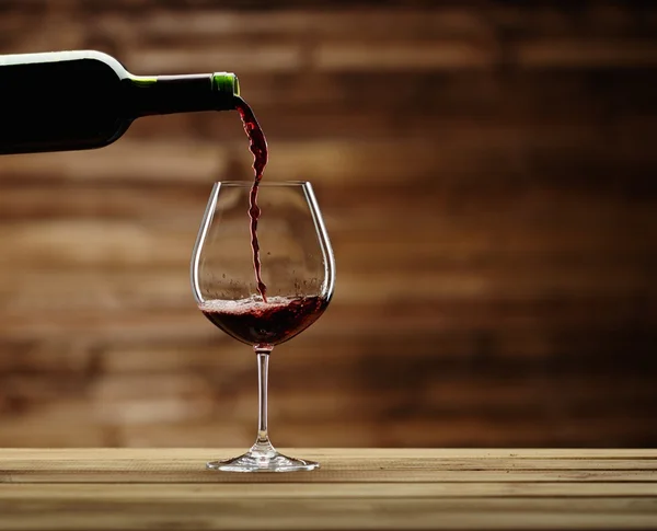 Pouring red wine into the glass against wooden background — Stock Photo, Image