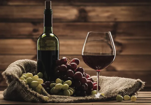 Botella de vino tinto, copa y uva en un saco en interior de madera —  Fotos de Stock
