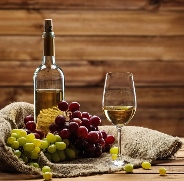 Botella de blanco rojo, vidrio y uva en un saco en el interior de madera —  Fotos de Stock