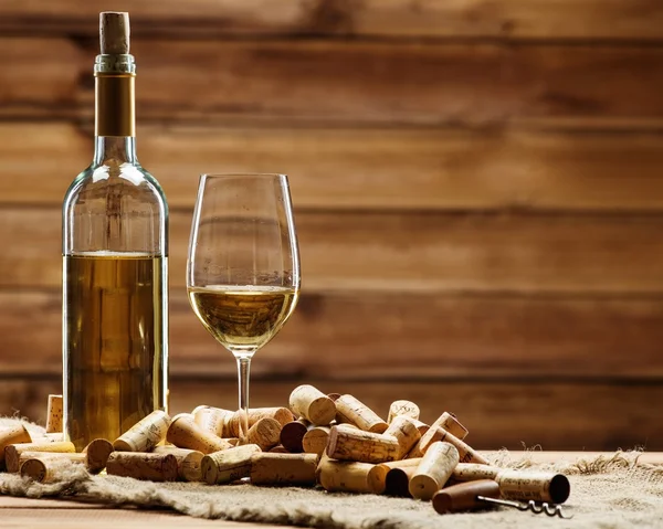 Garrafa e copo de vinho branco em uma mesa de madeira entre rolhas — Fotografia de Stock