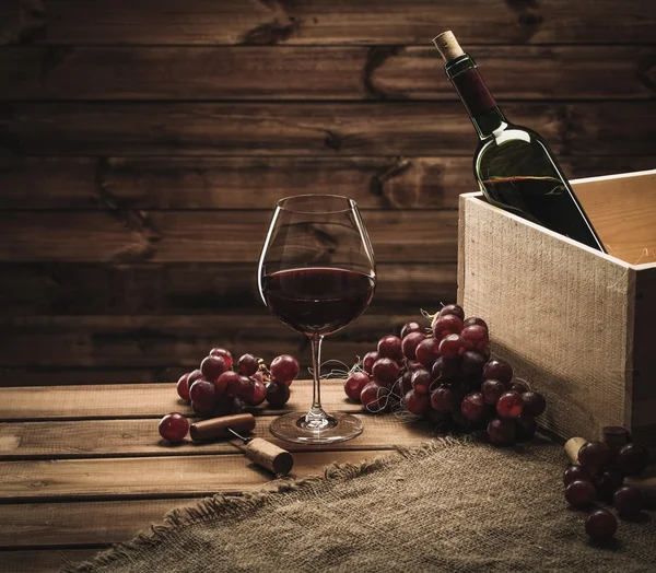 Garrafa, vidro e uva vermelha em uma mesa de madeira — Fotografia de Stock