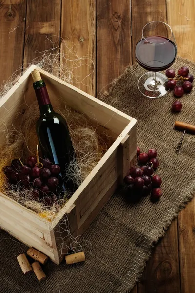 Bottiglia, bicchiere e uva rossa su un tavolo di legno — Foto Stock