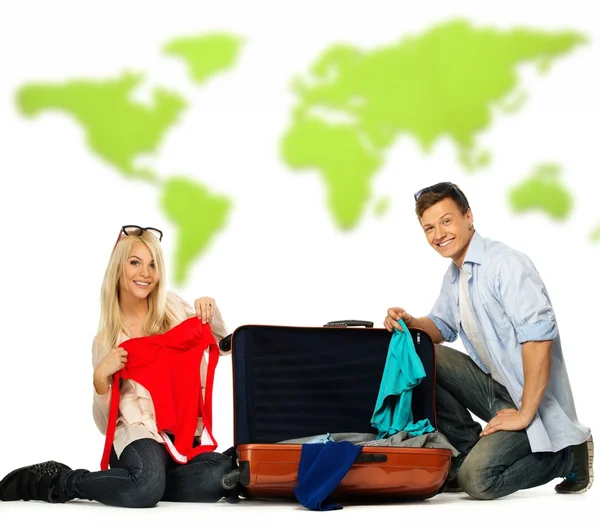 Young couple packing suitcase for a journey against world map — Stock Photo, Image