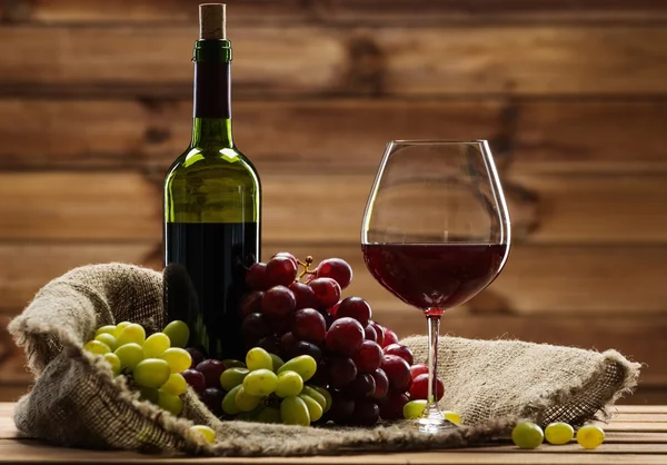 Botella de vino tinto, copa y uva en un saco en interior de madera Imagen De Stock