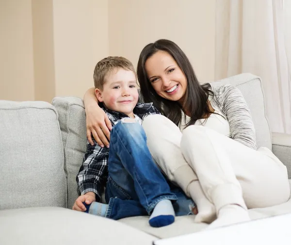 Feliz joven madre con su hijo en un sofá en el interior del hogar — Foto de Stock