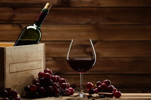 Botella, vidrio y uva roja sobre una mesa de madera — Foto de Stock