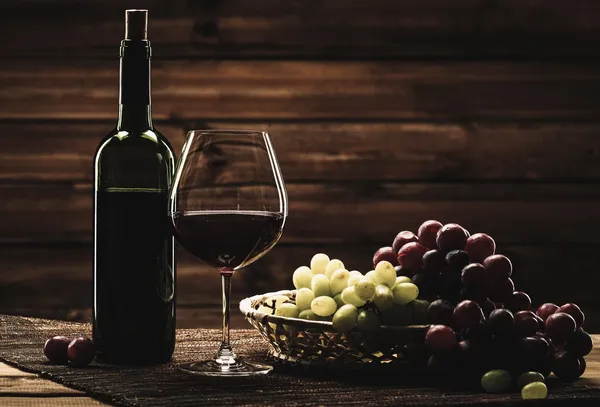 Μπουκάλι κόκκινο κρασί, γυαλί και σταφυλιών στο καλάθι σε ξύλινα εσωτερικών — Φωτογραφία Αρχείου