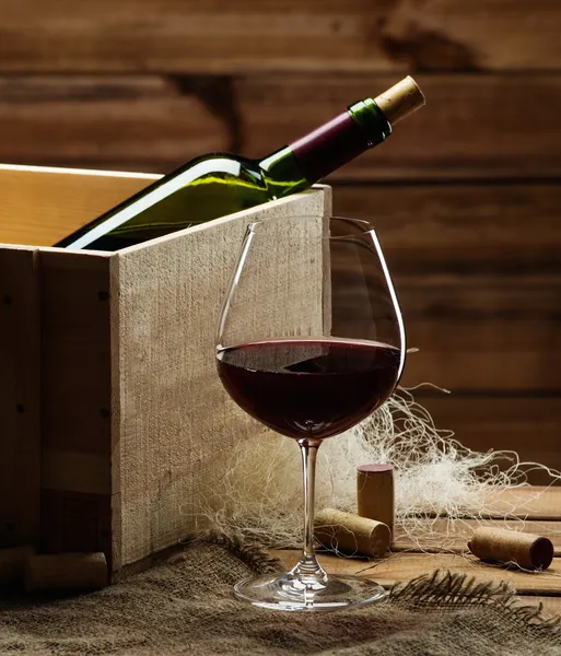 Láhve a sklenice červeného vína na dřevěný stůl — Stock fotografie