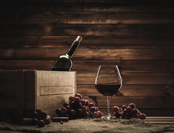 Botella, vidrio y uva roja sobre una mesa de madera — Foto de Stock