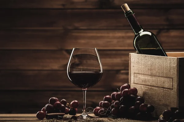Bottiglia, bicchiere e uva rossa su un tavolo di legno — Foto Stock