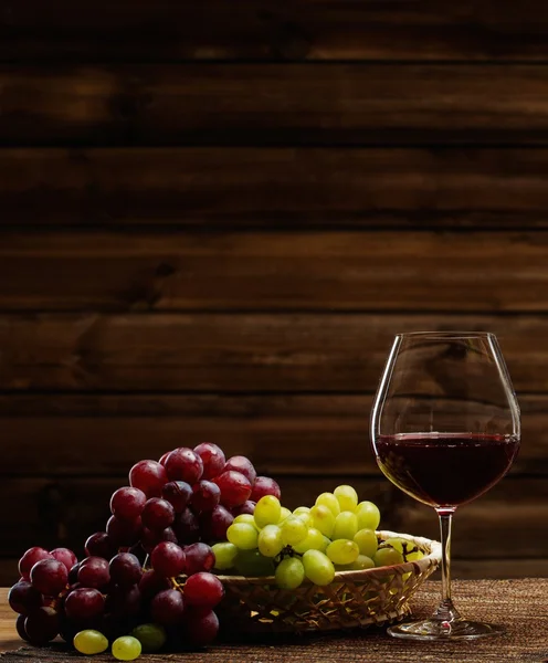 Copa de vino tinto y uva en cesta en interior de madera — Foto de Stock