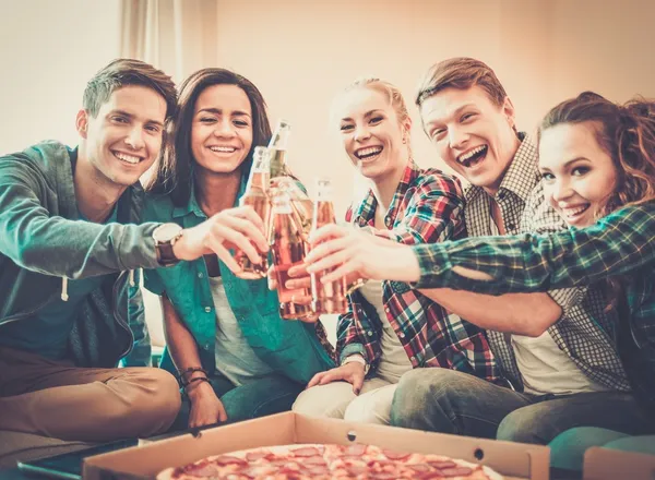 Grupo de jóvenes amigos multiétnicos con pizza y botellas de bebida celebrando en el interior del hogar — Foto de Stock