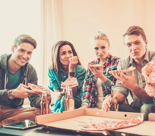 Группа молодых многонациональных друзей с пиццей и бутылками напитков празднуют в интерьере дома — стоковое фото