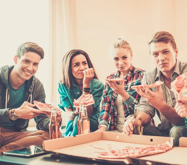 Grupo de jovens amigos multi-étnicos com pizza e garrafas de bebida comemorando em casa interior — Fotografia de Stock