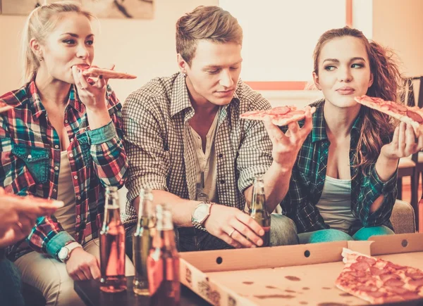 Grupo de jóvenes amigos con pizza y botellas de bebida celebrando en el interior del hogar — Foto de Stock