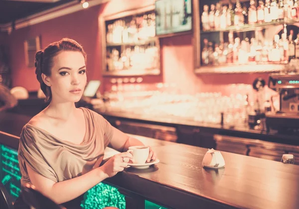 Beautiful young woman with cup of coffee near bar — Stock Photo, Image