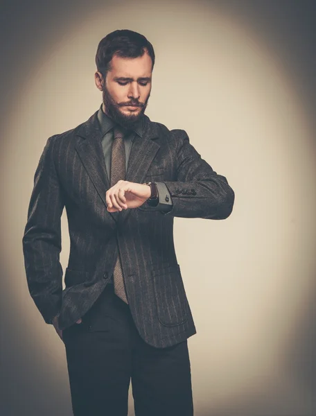 Красивый, хорошо одетый мужчина с бородой смотрит на свои наручные часы — стоковое фото
