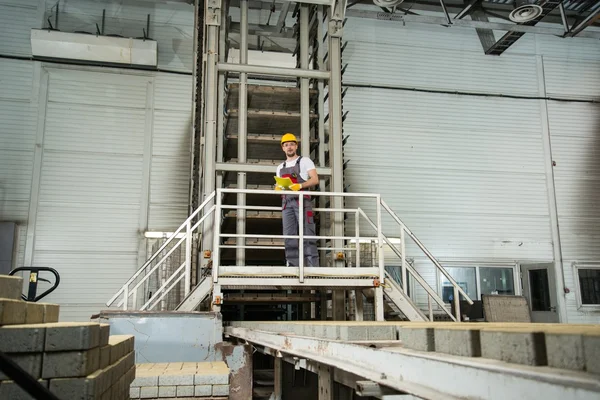 Man in a safety hat taking notes on a factory — Stock Photo, Image