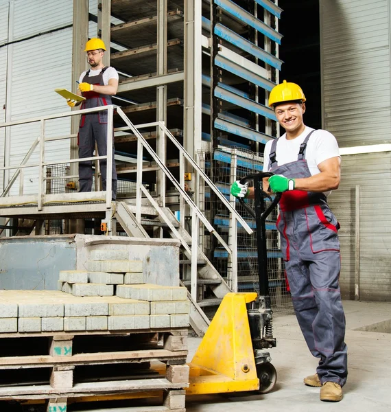 Young worker moving paving stones with pallet truck on a factory — Stock Photo, Image