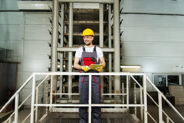 Man in a safety hat taking notes on a factory — Stock Photo, Image