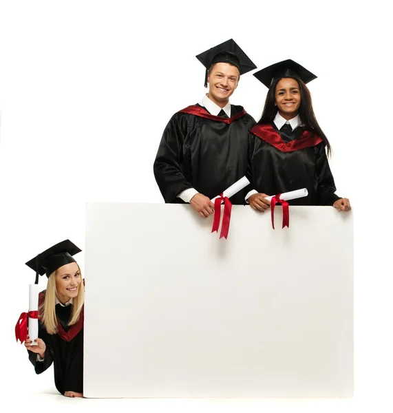 Grupo étnico multi de estudantes jovens graduados com placa de aviso em branco — Fotografia de Stock