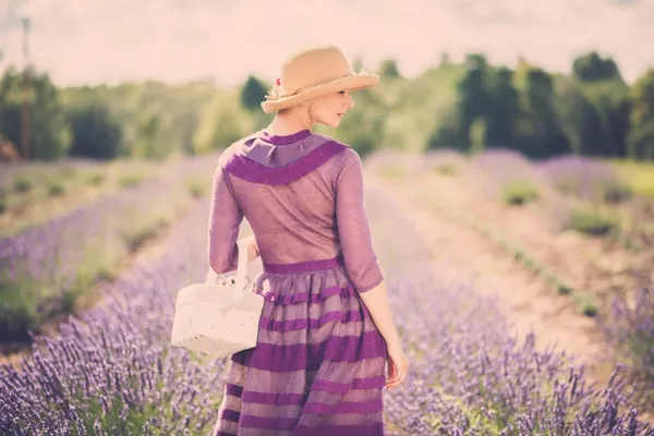 Donna in abito viola e cappello con cesto in campo di lavanda — Foto Stock