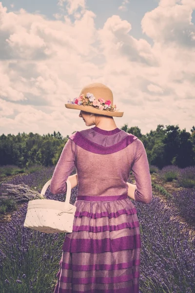 Donna in abito viola e cappello con cesto in campo di lavanda — Foto Stock