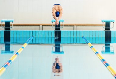 Young muscular swimmer jumping from starting block in a swimming pool clipart