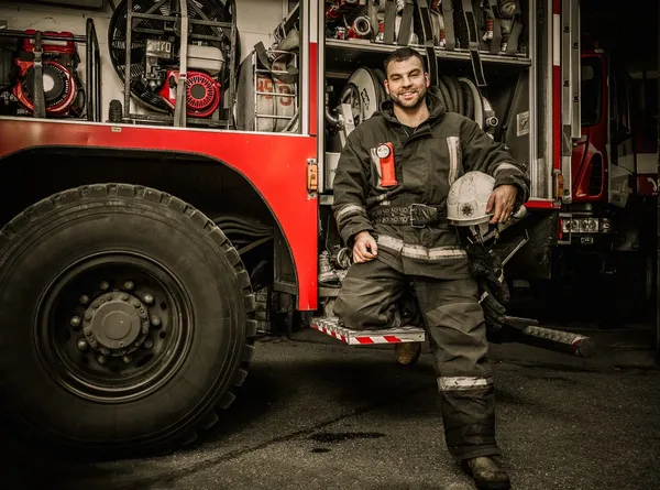 Bombeiro alegre perto de caminhão com equipamento — Fotografia de Stock