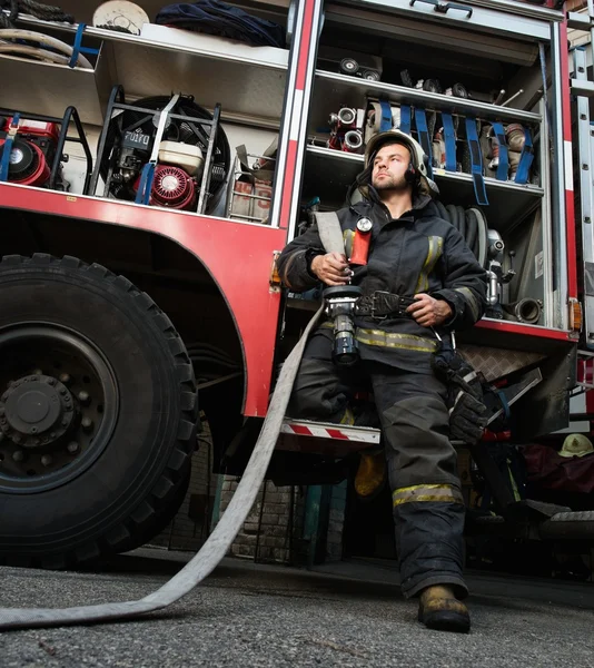 Пожежник біля вантажівки з обладнанням з водяним шлангом над плечем — стокове фото