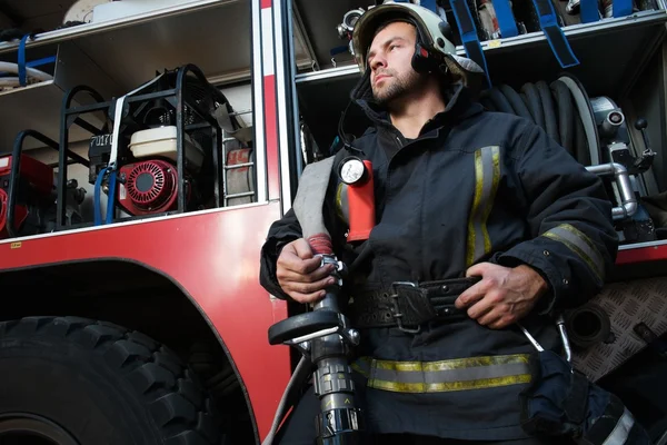 Pompiere vicino camion con attrezzature con tubo dell'acqua sopra la spalla — Foto Stock