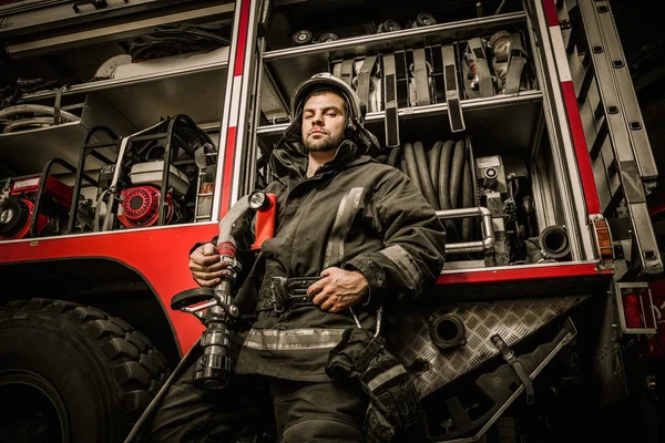 Пожежник біля вантажівки з обладнанням з водяним шлангом над плечем — стокове фото