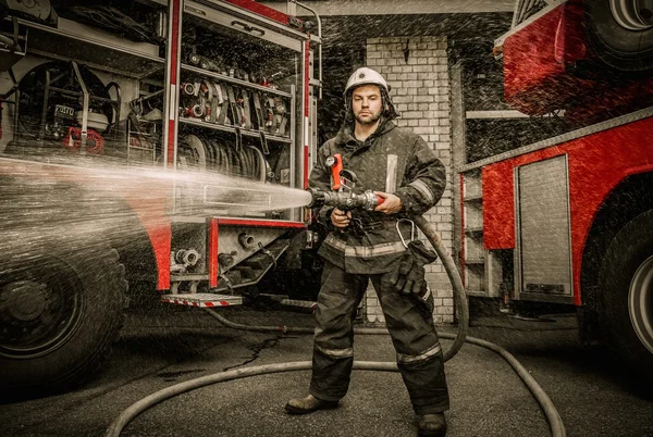 Bombero sosteniendo manguera de agua cerca de camión con equipo —  Fotos de Stock