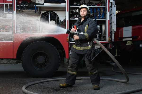 Feuerwehrmann hält Wasserschlauch neben LKW mit Gerät — Stockfoto