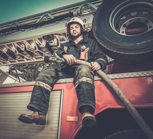 Firefighter sitting on a firefighting truck with water hose — Stock Photo, Image