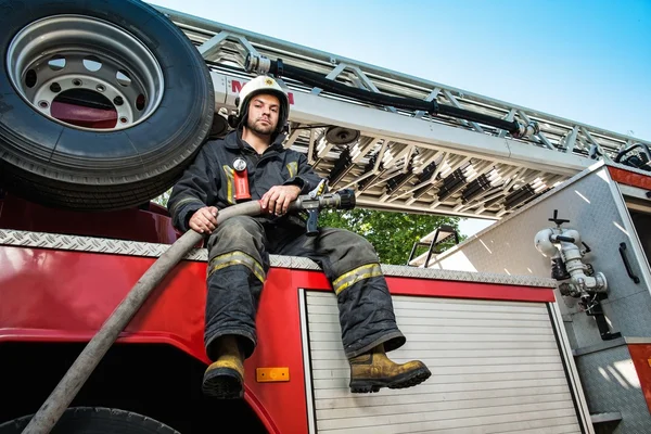 Firefighter sitting on a firefighting truck with water hose — Stock Photo, Image