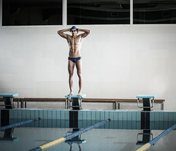 Jovem nadador muscular de pé no bloco de partida em uma piscina — Fotografia de Stock