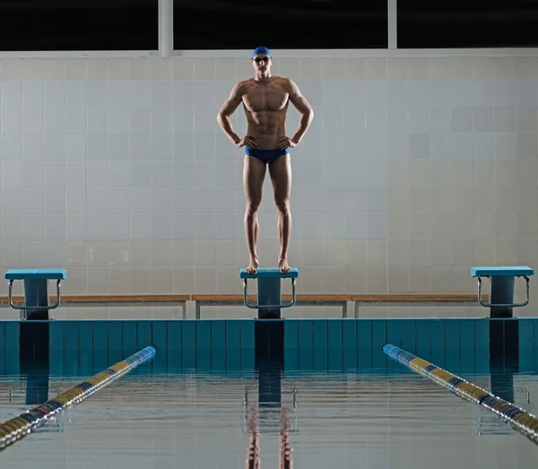 Young muscular swimmer standing on starting block in a swimming pool — Stock Photo, Image