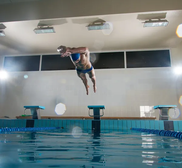 Young muscular swimmer jumping from starting block in a swimming pool — Stock Photo, Image