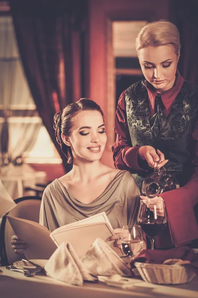 Mooie jonge meisje in restaurant en serveerster gieten wijn — Stockfoto