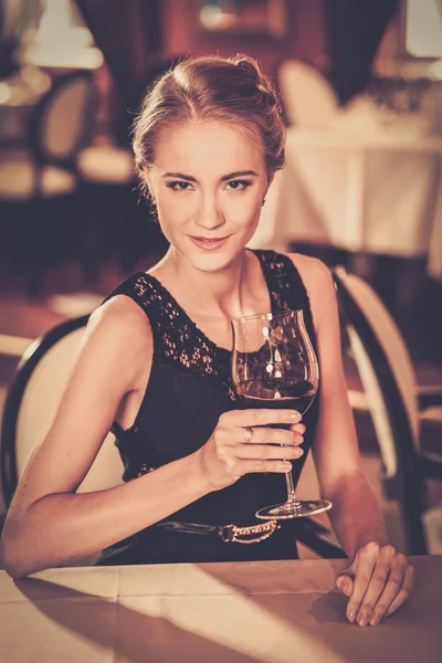 Beautiful young girl with glass of red wine alone in a restaurant — Stock Photo, Image