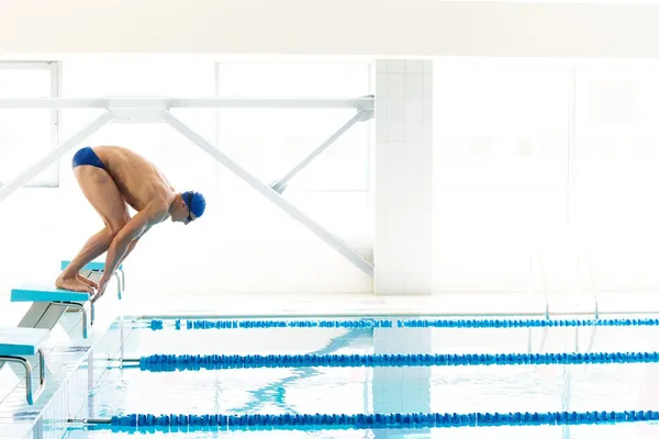 Mladý svalnatý plavec v nízké poloze na startovní blok v bazénu — Stock fotografie