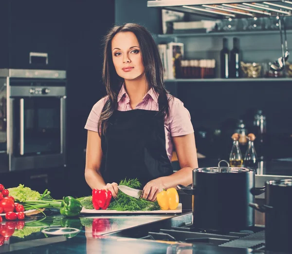 Vrolijke jonge vrouw in schort op moderne keuken snijden groenten — Stockfoto