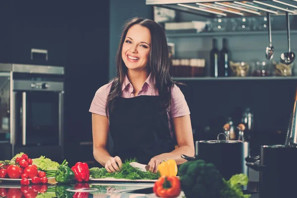 Felice giovane donna in grembiule sulla cucina moderna tagliare le verdure — Foto Stock