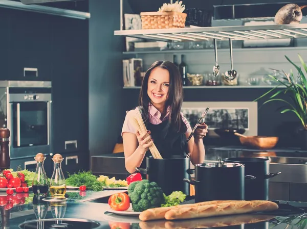 Mujer joven sonriente cocinando espaguetis en una cocina moderna — Foto de Stock