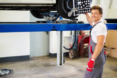 Young serviceman checking wheel alignment  in a car workshop  clipart
