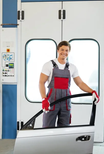 Cheerful serviceman with car door near paint booth in a car body workshop — Stock Photo, Image