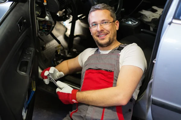 Cheerful mechanic with wrench fixing something in a car interior — Stock Photo, Image