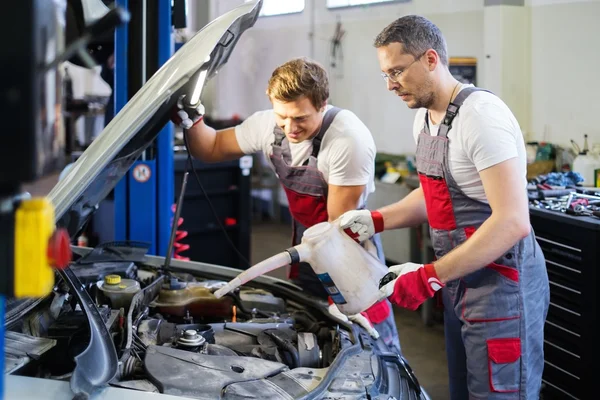 Dos mecánicos agregando nivel de aceite en un taller de automóviles — Foto de Stock