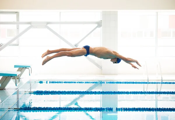 Joven nadador muscular saltando desde el bloque de partida en una piscina — Foto de Stock